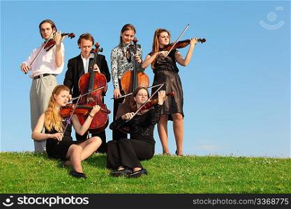 group of violinists play on grass against sky