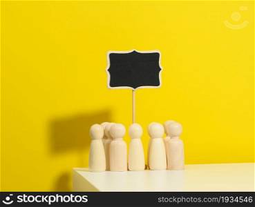 group of wooden figurines and a blank signpost on a yellow background. The concept of gathering people to express their will, demonstration, rally and strike