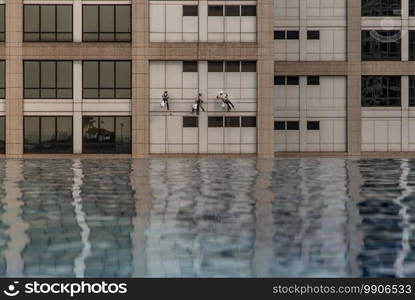 Group of workers cleaning windows service on high rise office building with reflection from swimming pool. Selective focus.