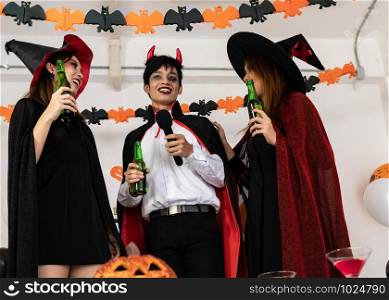 Group of young adult and teenager people celebrating a Halloween party carnival Festival in Halloween costumes drinking alcohol beer singing a song and dancing.