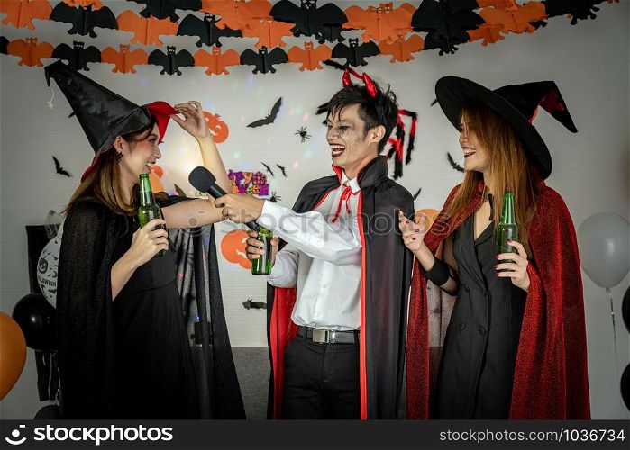 Group of young adult and teenager people celebrating a Halloween party carnival Festival in Halloween costumes drinking alcohol beer singing a song and dancing.