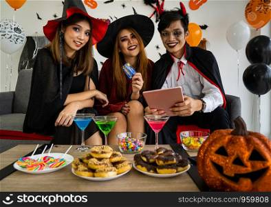 Group of young adult and teenager people celebrating a Halloween party carnival Festival in Halloween costumes and making online shopping with tablet and credit card