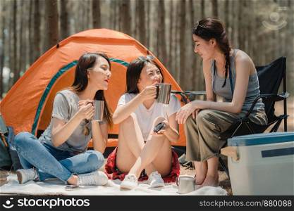 Group of young Asian friends camping or picnic together in forest, teenager female enjoy moment talking in front of their tent. Women do adventure activity and travel on holidays vacation in summer.