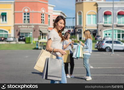 Group of young Asian woman shopping in an outdoor market with shopping bags in their hands. Young Asian women show what they got in shopping bag under warm sunlight. Group outdoor shopping concept.