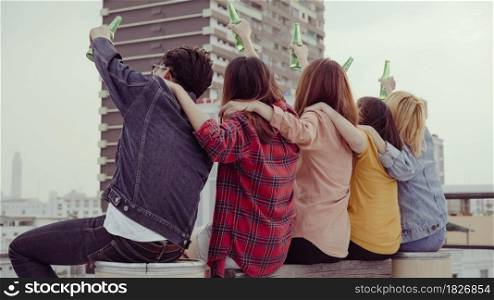Group of young asian women and man people dancing and raising their arms up in air to the music played by dj at sunset urban party on rooftop. Young asian girls and boy friends hanging out with drinks