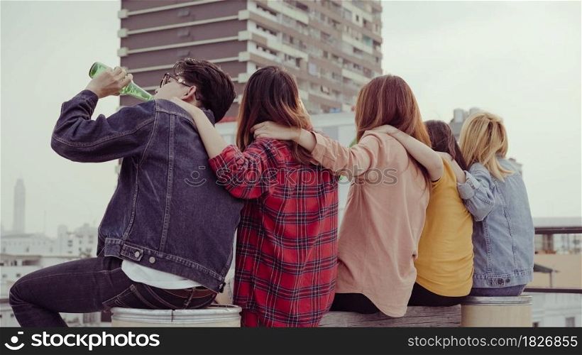 Group of young asian women and man people dancing and raising their arms up in air to the music played by dj at sunset urban party on rooftop. Young asian girls and boy friends hanging out with drinks