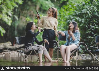 Group of young asian women drink beer in their chairs and soaked their feet in the stream while c&ing in the nature park, They are enjoy to talking and laugh fun together.