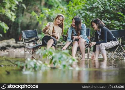 Group of young asian women drink beer in their chairs and soaked their feet in the stream while c&ing in the nature park, They are enjoy to talking and laugh fun together.