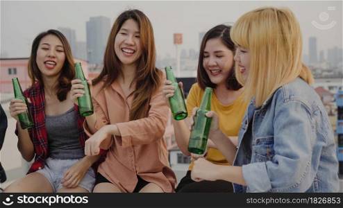 Group of young asian women people dancing and raising their arms up in air to the music played by dj at sunset urban party on rooftop. Young asian girls friends hanging out with drinks.