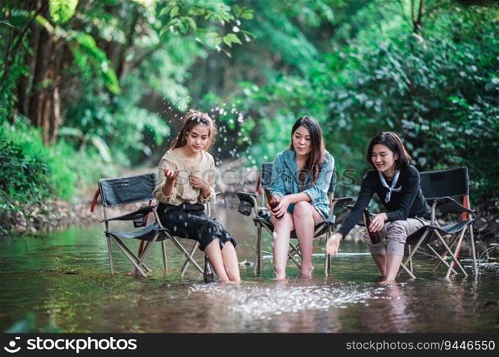 Group of young asian women sitting in their chairs with beer and enjoy to splashing water in the stream while c&ing in the nature park, They are talking and laugh fun together.