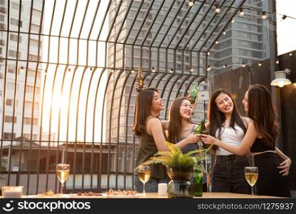 Group of young beautiful happy asian women holding bottle of beer chat together with friends while celebrating dance party on outdoor rooftop nightclub with copy space for advertising.
