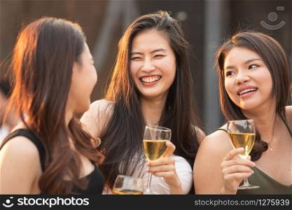 Group of young beautiful happy asian women holding glass of wine chat together with friends while celebrating dance party on outdoor rooftop nightclub,leisure lifestyle of young friendship concept.