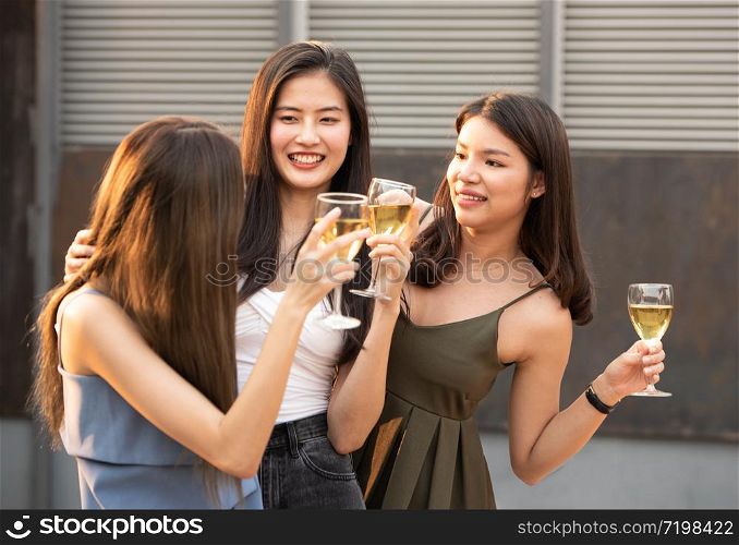 Group of young beautiful happy asian women holding glass of wine chat together with friends while celebrating dance party on outdoor rooftop nightclub,leisure lifestyle of young friendship concept.