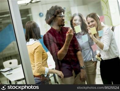 Group of young business people discussing in front of glass wall using post it notes and stickers at startup office