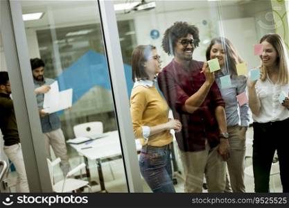 Group of young business people discussing in front of glass wall using post it notes and stickers at startup office