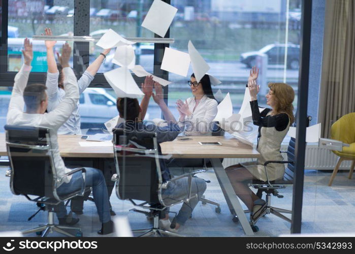 Group of young business people throwing documents and looking happy while celebrating success at their working places in startup office