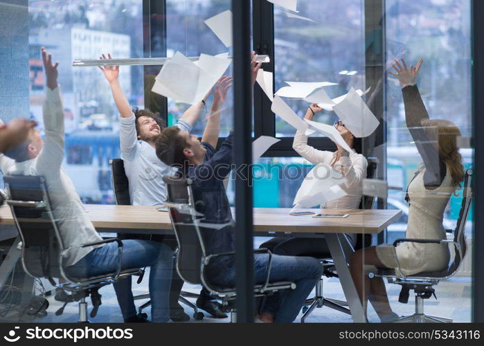 Group of young business people throwing documents and looking happy while celebrating success at their working places in startup office