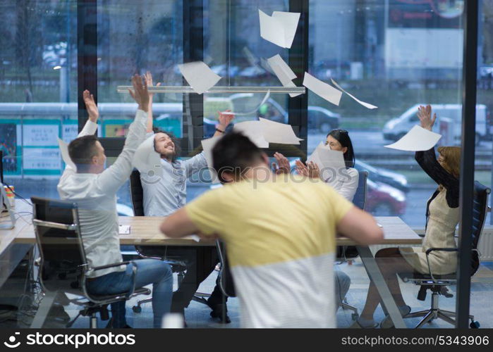 Group of young business people throwing documents and looking happy while celebrating success at their working places in startup office