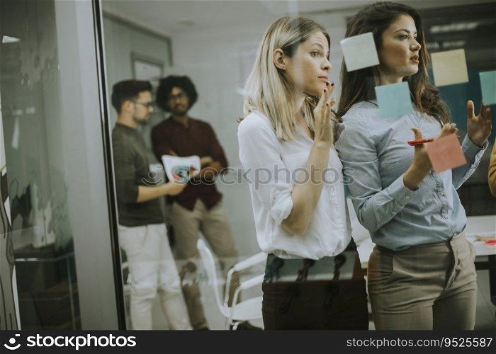 Group of young business women discussing in front of glass wall using post it notes and stickers at startup office