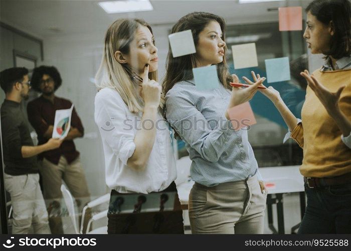 Group of young business women discussing in front of glass wall using post it notes and stickers at startup office