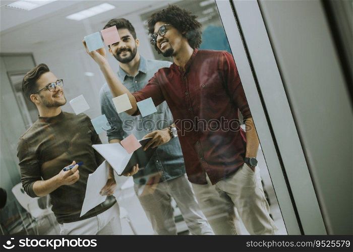Group of young businessmen discussing in front of glass wall using post it notes and stickers at startup office