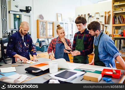 Group of young craftspeople using digital tablet in book arts workshop