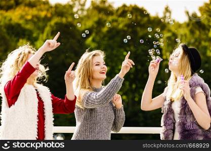 Group of young fashion women best friends having fun together blowing bubbles with toy bubble wand while enjoying sunny day outdoors. Happiness and carefree concept.. Women blowing soap bubbles, having fun