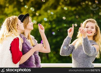Group of young fashion women best friends having fun together blowing bubbles with toy bubble wand while enjoying sunny day outdoors. Happiness and carefree concept.. Women blowing soap bubbles, having fun