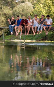 group of young friends enjoying watermelon while sitting on the wooden bridge over the river in beautiful nature