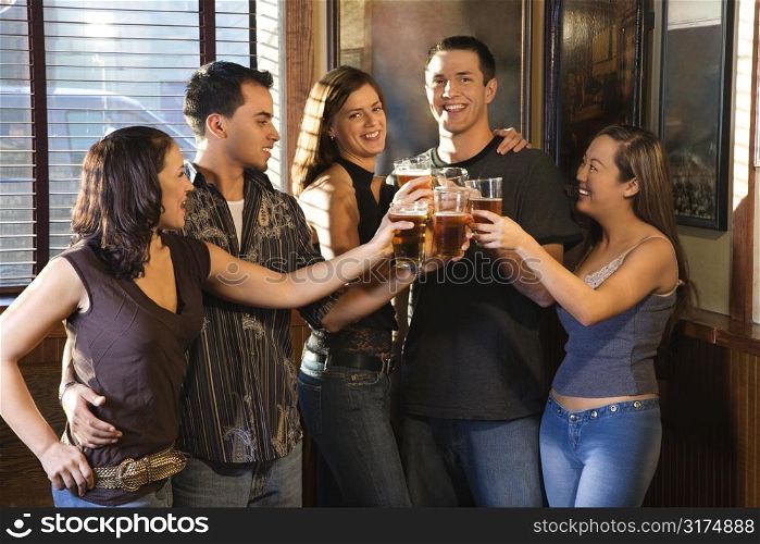 Group of young friends hanging out in pub and toasting with their beers.