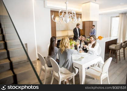 Group of young friends having dinner at home and toasting with white wine