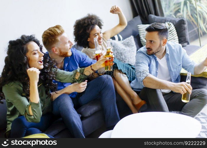 Group of young friends looking at the TV, drinking cider and having fun in the room