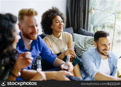 Group of young friends looking at the TV, drinking cider and having fun in the room