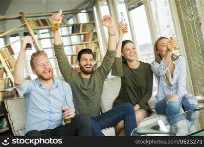 Group of young friends looking at the TV, drinking cider and having fun  in the room