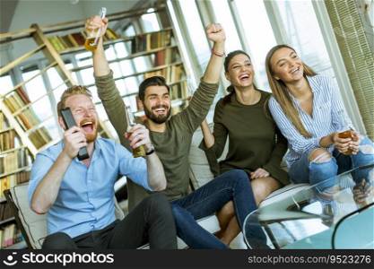 Group of young friends looking at the TV, drinking cider and having fun  in the room