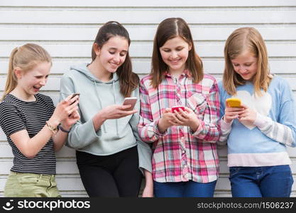 Group Of Young Girls Outdoors Looking At Messages On Mobile Phones