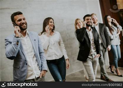 Group of young good looking people standing together over wall background and using mobile phone