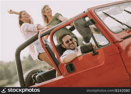 Group of young happy people enjoying road trip in red convertible and smiling