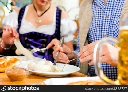 group of young men and women in traditional Bavarian Tracht having a breakfast with white veal sausage, pretzel, and beer