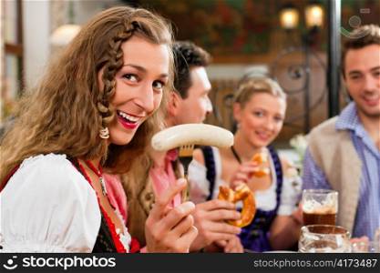 group of young men and women in traditional Bavarian Tracht having a breakfast with white veal sausage, pretzel, and beer