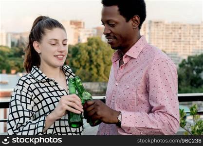 Group of young multi-ethnic friends having fun with bottles of drink celebrating at outdoor rooftop. Friendship concept