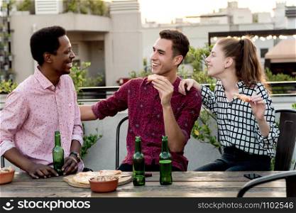 Group of young multi-ethnic friends with pizza and bottles of drink celebrating at outdoor rooftop. Friendship concept