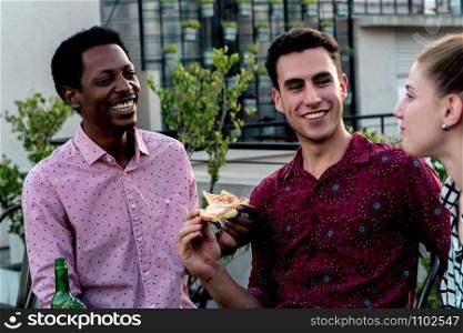 Group of young multi-ethnic friends with pizza and bottles of drink celebrating at outdoor rooftop. Friendship concept