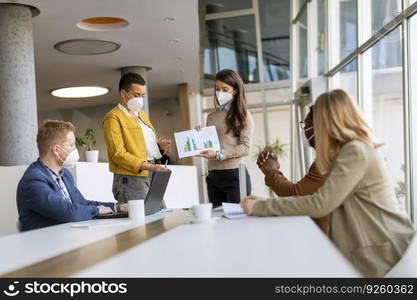 Group of young multiethnic business people working together with facial protective masks and preparing new project on a meeting in office