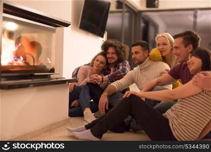 group of young multiethnic couples sitting on the floor in front of fireplace at cold winter night
