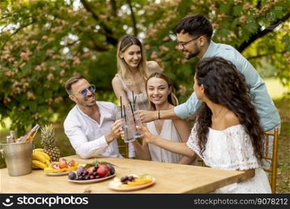 Group of young people cheering with fresh lemonade and eating fruits in the garden