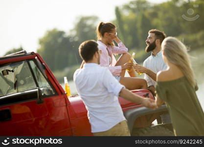 Group of young people drinking and having fun by car outdoor on a sunny hot summer day