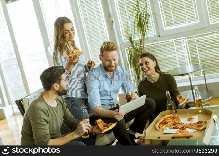 Group of young people eating pizza, drinking cider and watching digital tablet in the room