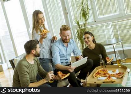Group of young people eating pizza, drinking cider and watching digital tablet in the room