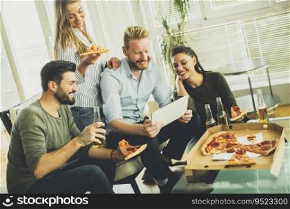 Group of young people eating pizza, drinking cider and watching tablet in the room